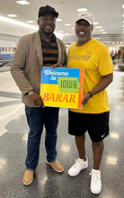 Derrick and Bakar at airport with a sign welcoming Bakar