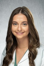 picture of Riley, long dark hair and wearing white physician coat