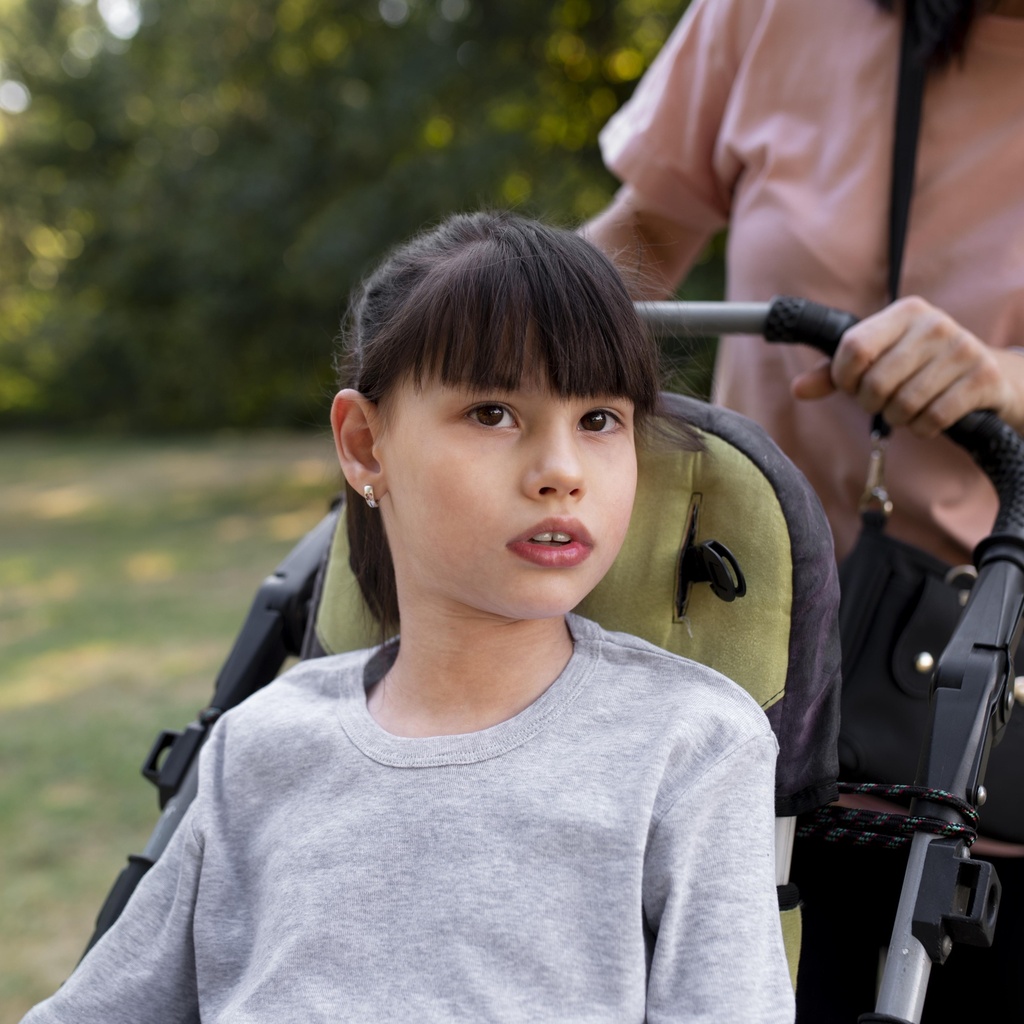 child with wheelchair being pushed by women outside in nature