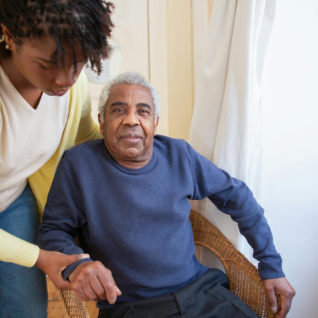 man in chair, women helping get him up from chair